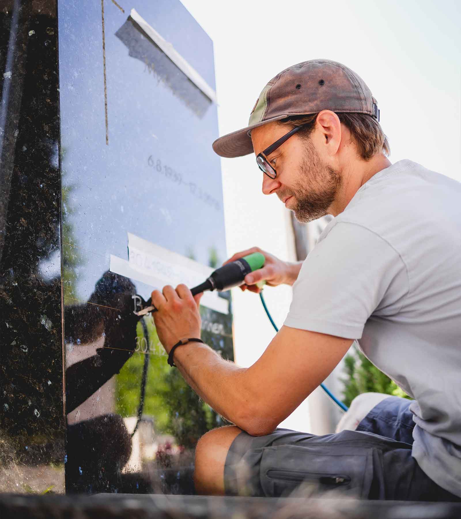 Florian arbeitet mit einem Meisel direkt im freien an einem Grabstein.