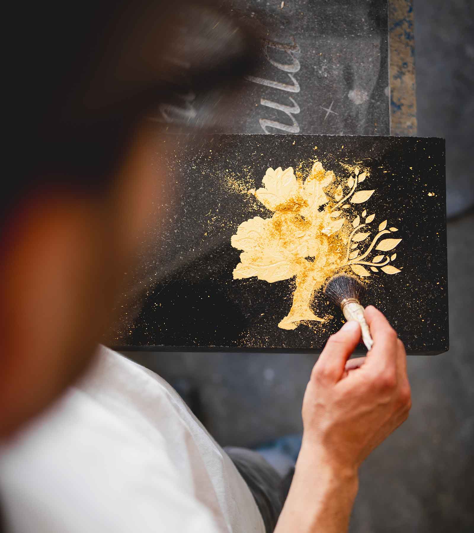 Florian bringt goldene Pigmente auf eine schwarze Grabplatte auf, um Details hervorzuheben.